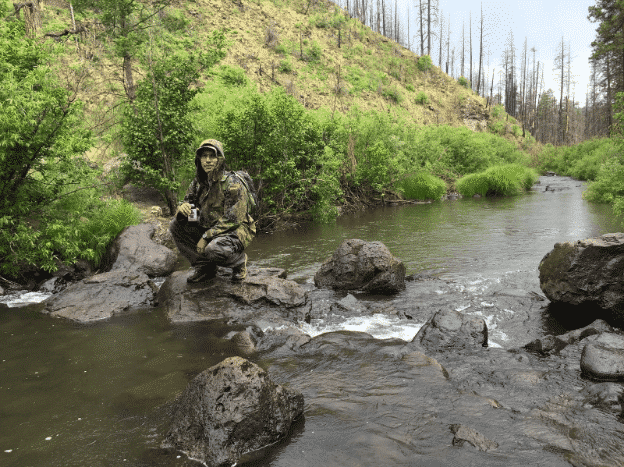 soldier in camouflage sitting on rocks by a stream