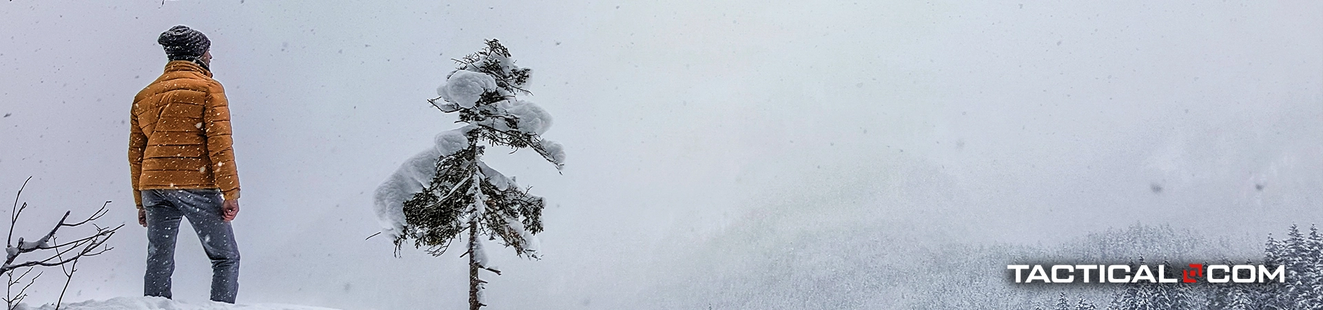 man in winter clothing standing near a tree while it's snowing