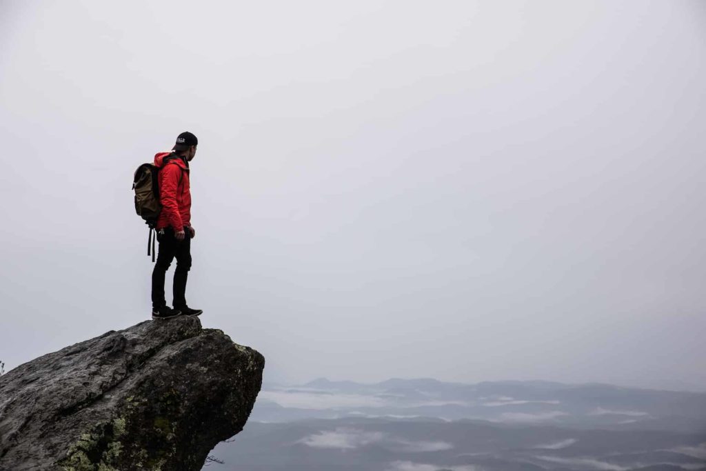 man with backpack standing on cliff